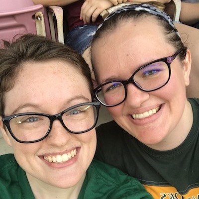 CJ and their wife Meg sit in a sports stadium, heads pressed together